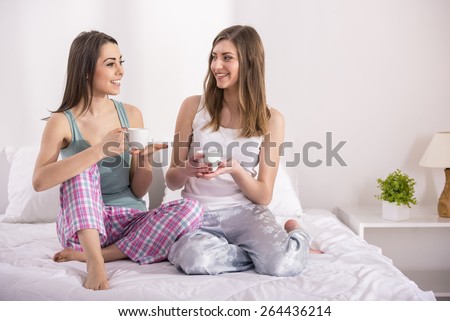 Pajama party. Young beauty girls in pajamas drinking a cup of tea in bed at home. Pajamas party