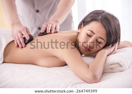 Male masseur doing massage on woman body with zen basalt stones in the spa salon.