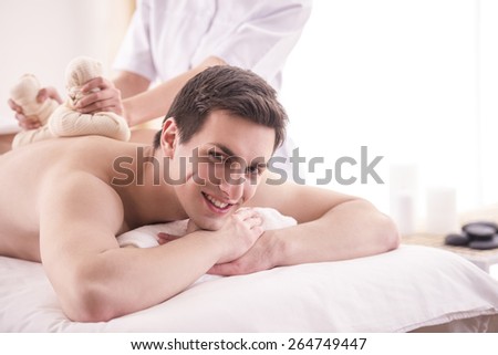 Female masseur doing massage on male body with spa herbal balls in the spa salon.