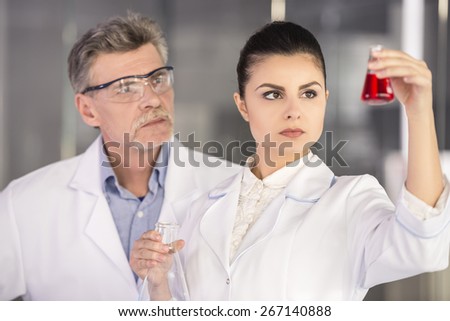 Senior chemistry professor and his assistant looking on flask with red fluid  in  laboratory.