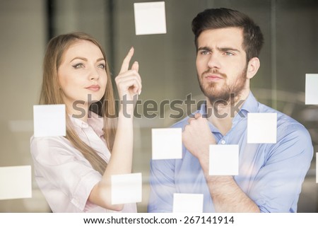 Young businessman and businesswoman working on new project with many sticky notes on glass screen in office.