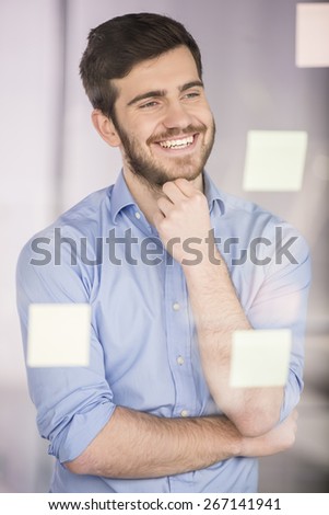 Young businessman working on new project with many sticky notes on glass screen in office.