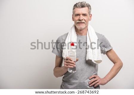 Smiling senior man in T-shirt on neck towel with bottle water on grey background. Foto stock © 