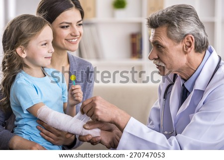 Male pediatrician is  checking bandage of girl broken arm.