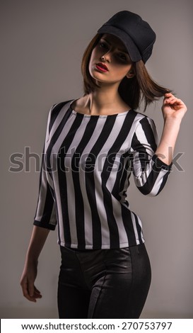 Young beauty woman in black-white shirt and in cap on grey background.