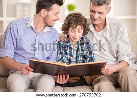 Generation portrait. Grandfather, father and son sitting and reading a book on sofa.