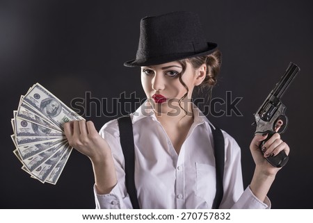 Beautiful and dangerous. Young female gangster holding the gun and counting money. isolated on dark background
