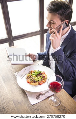 Businessman talking on phone and  holding notebook during a business lunch.