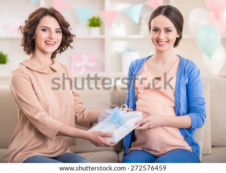 Young woman gives a gift to her pregnant friend.