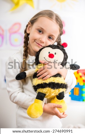 Little pretty  smiling girl in white  pullover with toy bee on colorful background.