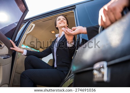 Young beautiful smiling businesswoman in suit coming out of her luxurious car.