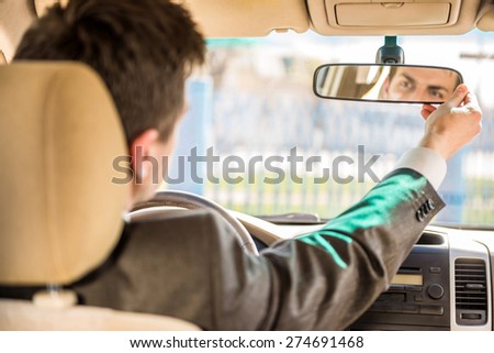 Young businessman in suit sitting in the car and looking in the front view mirror.