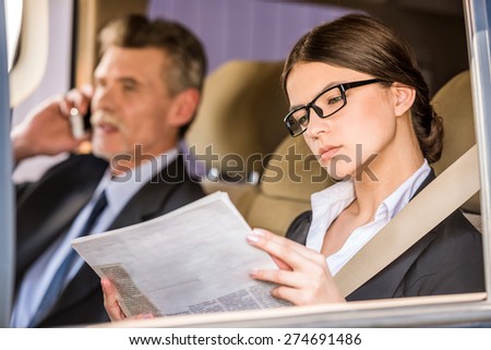 Mature businessman in suit sitting in the car with his beautiful personal assistant and talking on the phone.