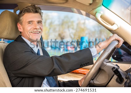 Mature confident smiling businessman  in suit driving his luxurious car.