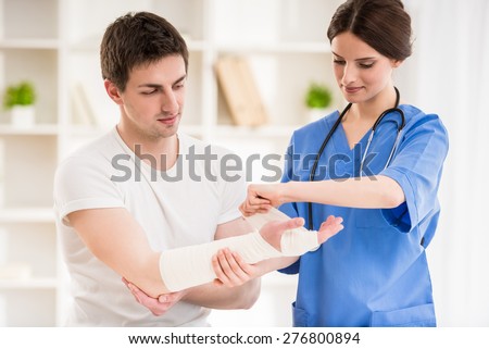 Young attractive female doctor with stethoscope  bandaging hand of male patient.