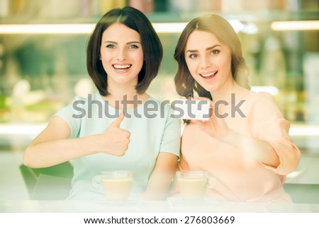 Young beautiful girl sitting in cafe with her friend and showing  new business card. focus on the model on the right