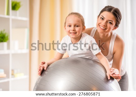 Mother and daughter doing physical exercises on fitness ball at home.