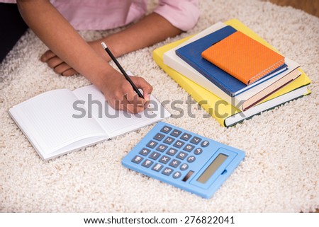 Close-up of girl laying on the white carpet and writing a homework.