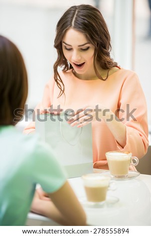 Young beautiful girl sitting in cafe with her friend and looking at the gift.