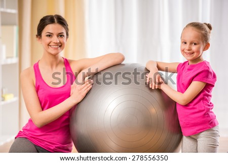 Mother and daughter doing physical exercises on fitness ball at home.