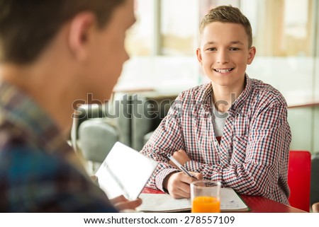 Male teenager sitting in cafe with friends, studying and drinking orange juice.