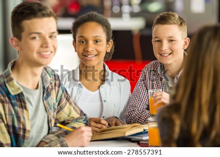 Smiling  teenagers sitting at the table in cafe, studying and drinking orange juice.