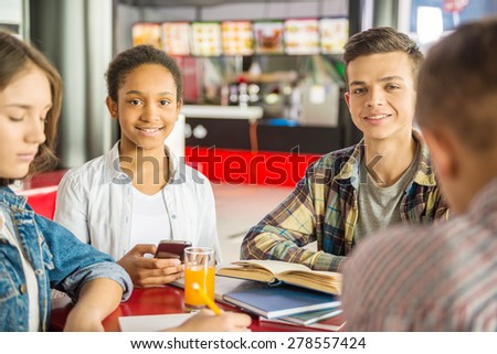 A group of teenagers sitting at the table in cafe, studying and drinking orange juice.