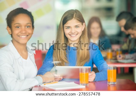 Two female friends sitting in cafe, using tablet and drinking orange juice.