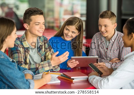 A group of teenagers sitting at the table in cafe, studying and using tablet.