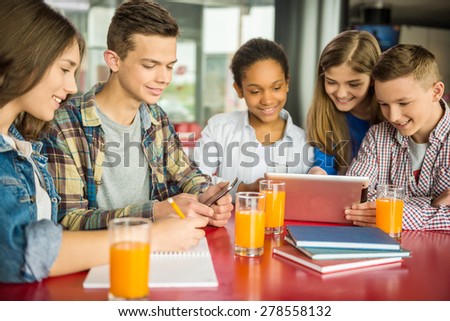 A group of teenagers sitting at the table in cafe, using digital tablet and drinking orange juice.