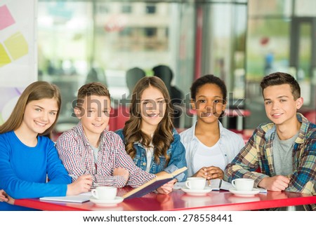A group of teenagers sitting at the table in cafe, studying and drinking tea.