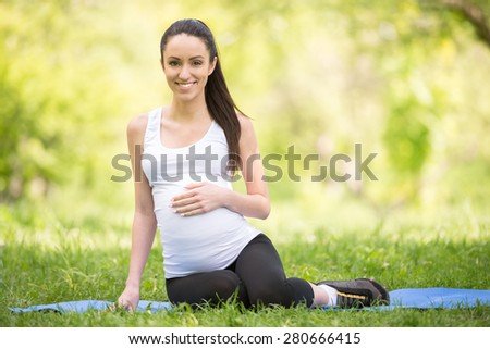 Beautiful pregnant woman sitting on rubber mat in summer park.