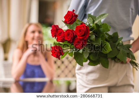 Young woman looking at man with flower bouquet behind the back.