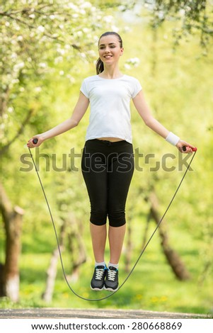 Young attractive athletic girl holding jumping-rope. Workout in the morning outdoors.