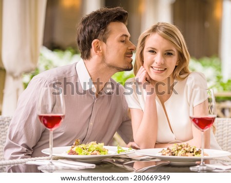 Young smiling couple enjoying the meal in gorgeous restaurant and drinking wine. Man whispering to woman.
