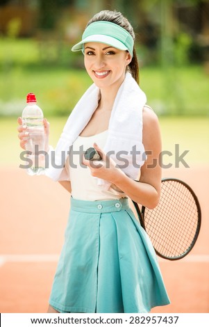 Female tennis player with towel on her shoulders drinking water after match.