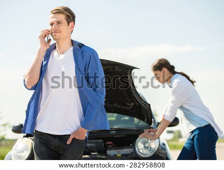 Young man standing near broken car and calling for help on phone.
