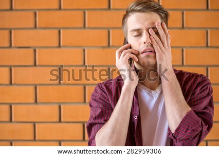 Young tired man talking on phone on brick wall background.