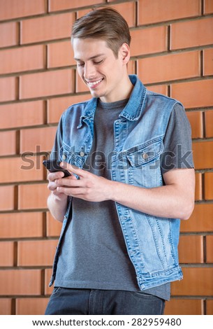 Young handsome man leaning at brick wall and looking at phone.