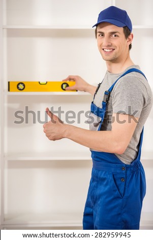Young smiling repairman using spirit level at home interior.