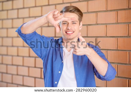 Handsome young man in smart casual wear showing frame gesture on brick wall background.