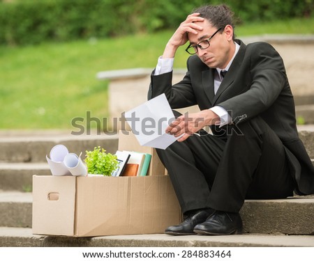Fired frustrated man in suit sitting near office at stairs.