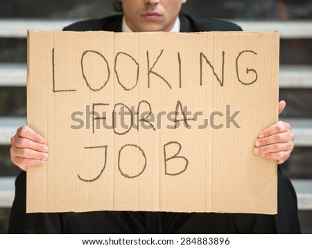 Close-up of man in suit sitting at stairs with sign in hands. Unemployed man looking for job.