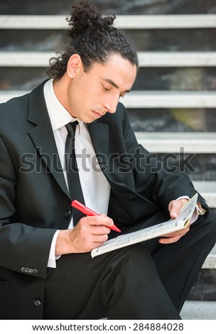 Man in suit sitting at stairs with  newspaper and searching job.