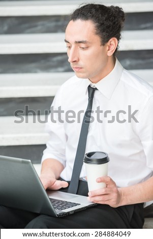 Man in suit sitting at stairs in office and using laptop.