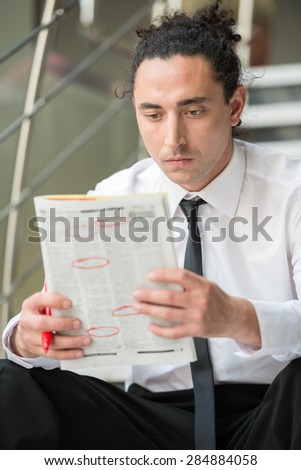 Man in suit sitting at stairs with  newspaper and searching job.