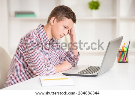 Boy sitting at desk with laptop and doing homework. Side view.