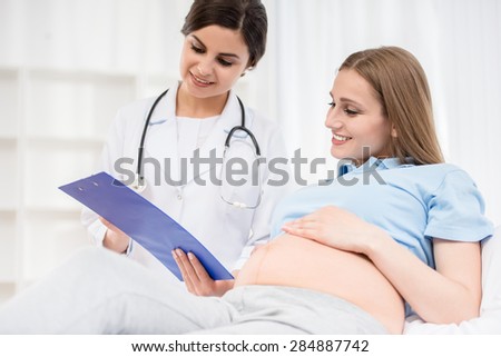 Pregnant woman lying down and talking with doctor at doctor\'s office.