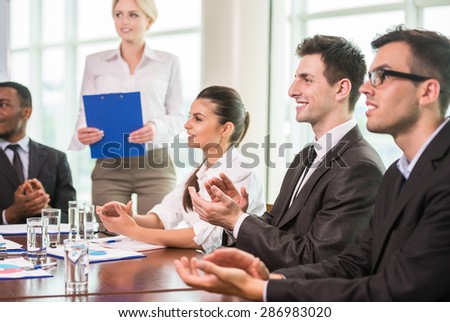 Young business people in suits sitting at meeting room and clapping to speaker.