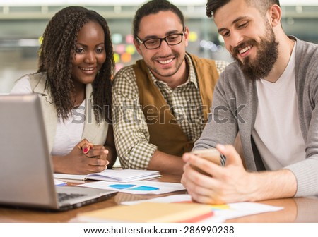 Group of creative young people dressed casual sitting at the table in office and looking at phone.